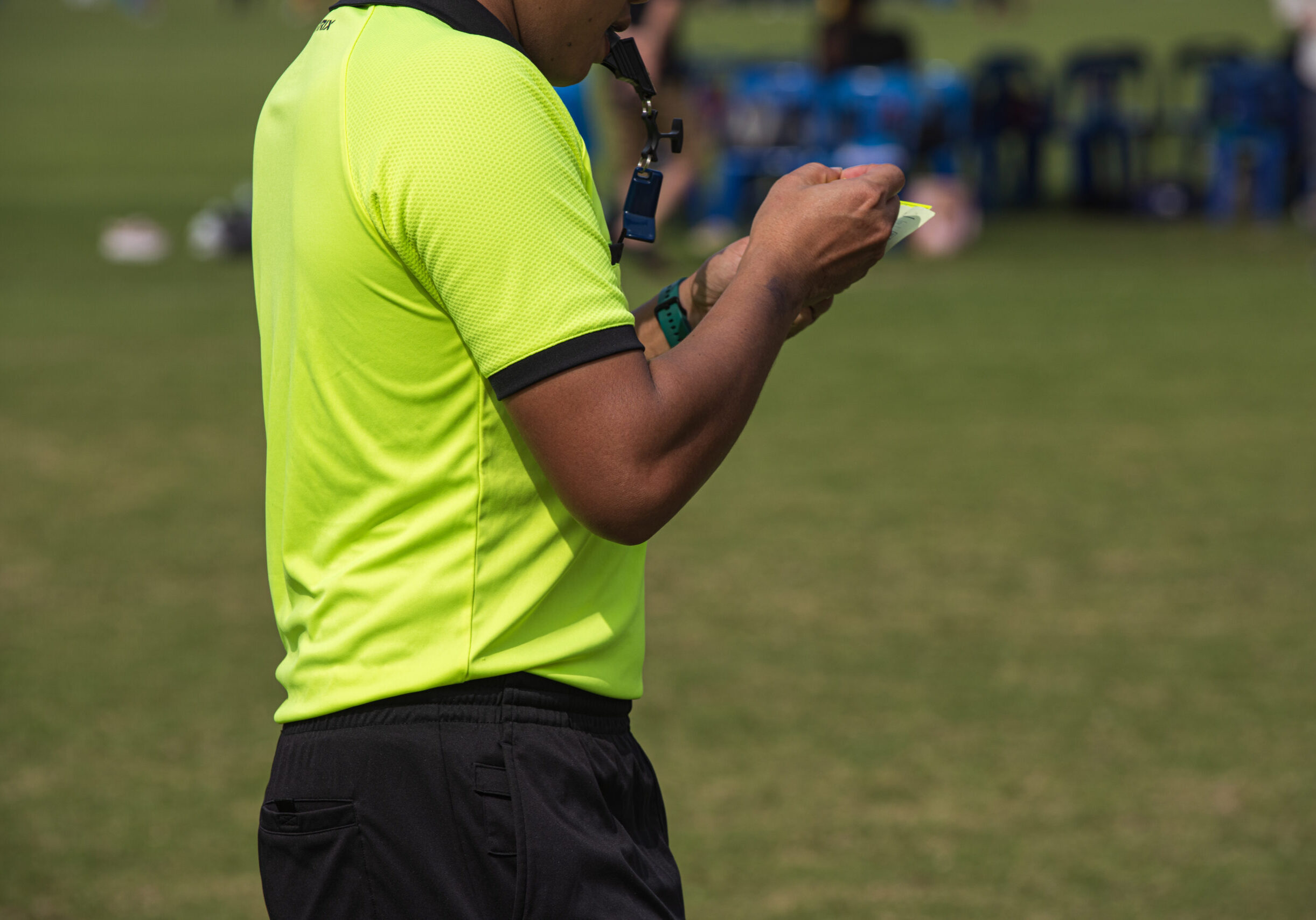 Professional soccer referee on a pitch of a youth soccer tournament. After team scores a goal, referee takes a note regarding to a match's score and a score player.